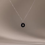 The Onyx Star Pendant Necklace in Sterling Silver features a round black onyx with a celestial star design, shown against a soft beige background.