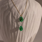 The Celestial Jade Pendant Necklace features two jade pendants on gold and silver chains, each with star and moon accents, creating an elegant celestial look. The necklace is showcased on a white bust.