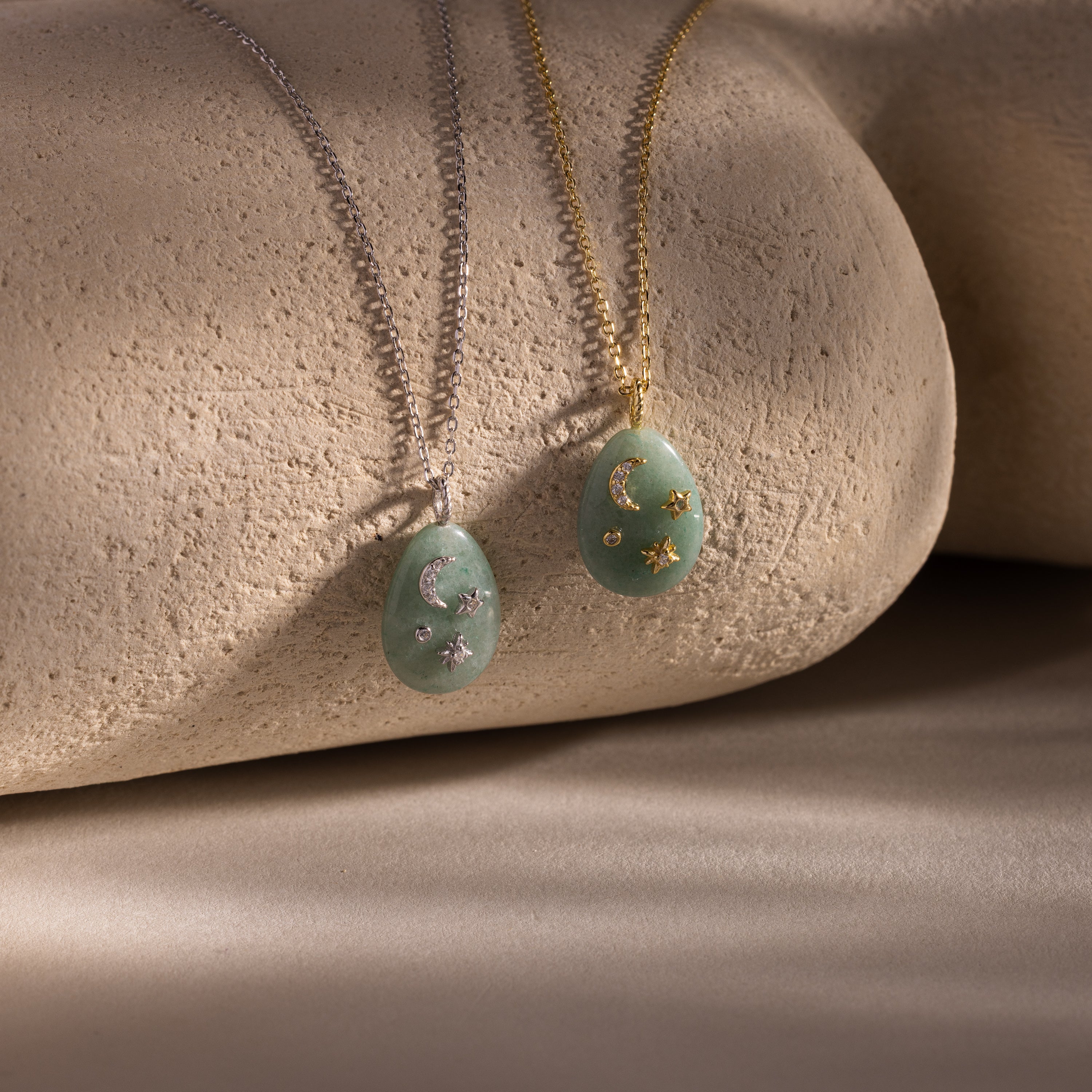 The Celestial Aventurine Pendant Necklace features crescent moon and star charms with green aventurine accents on silver and gold chains, beautifully displayed on textured stone.