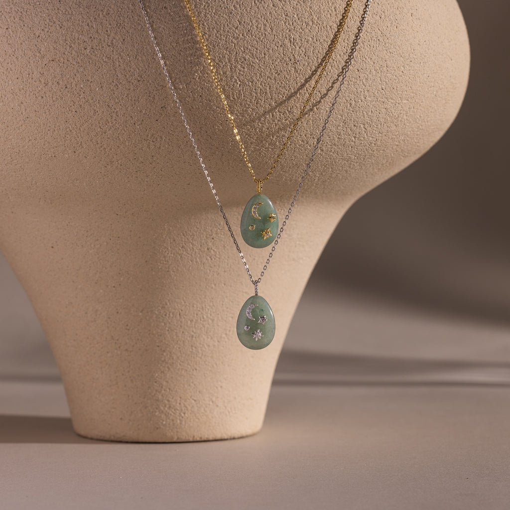 Two layered necklaces with oval green gemstone pendants, including the Celestial Aventurine Pendant Necklace, displayed on a textured beige mannequin.