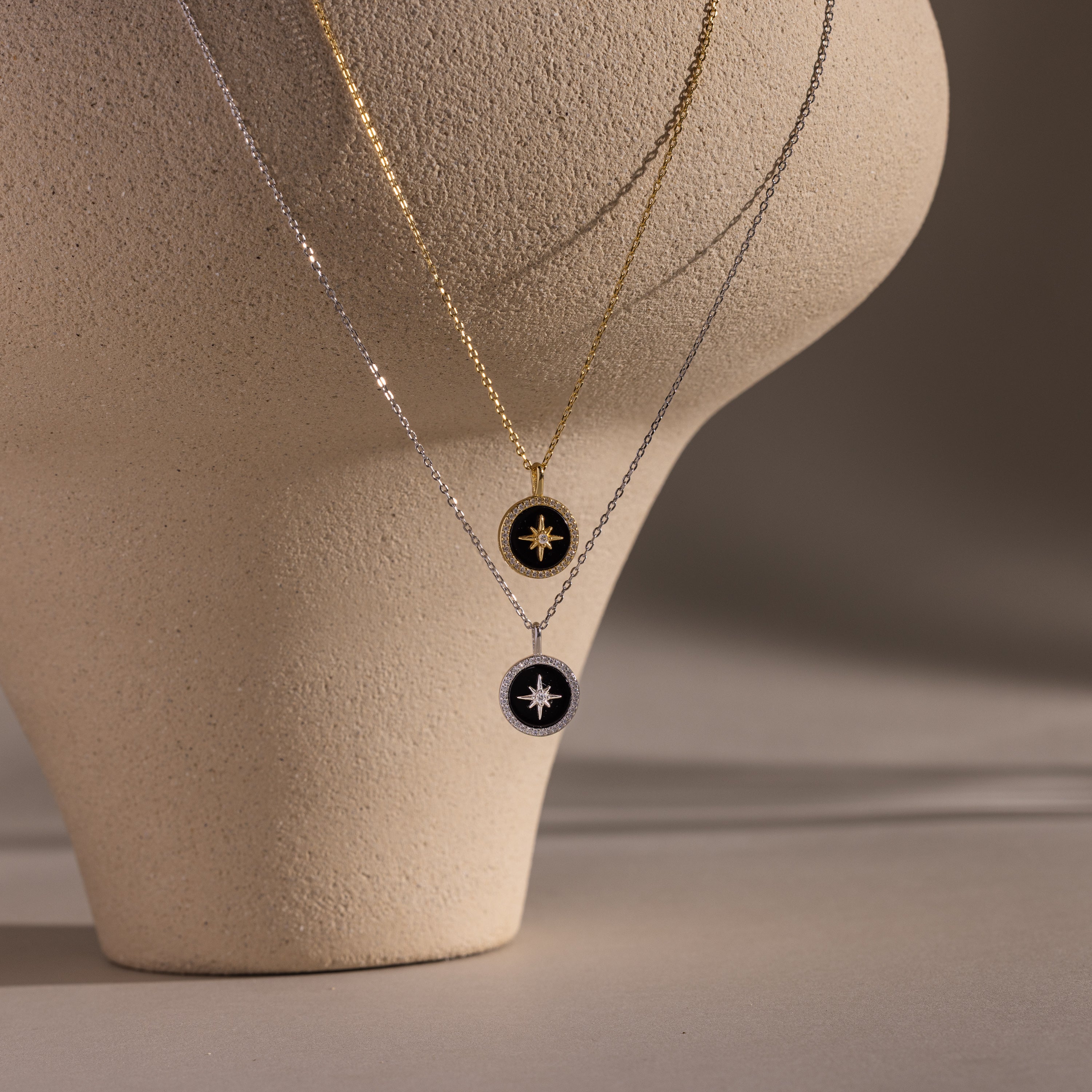 Two Onyx Star Pendant Necklaces hang on a textured beige sculpture, creating a striking display of celestial-inspired jewelry.