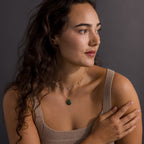 Woman with long wavy hair wearing a beige top and layered Celestial Gemstone Pendant Necklaces, gazing to the side.