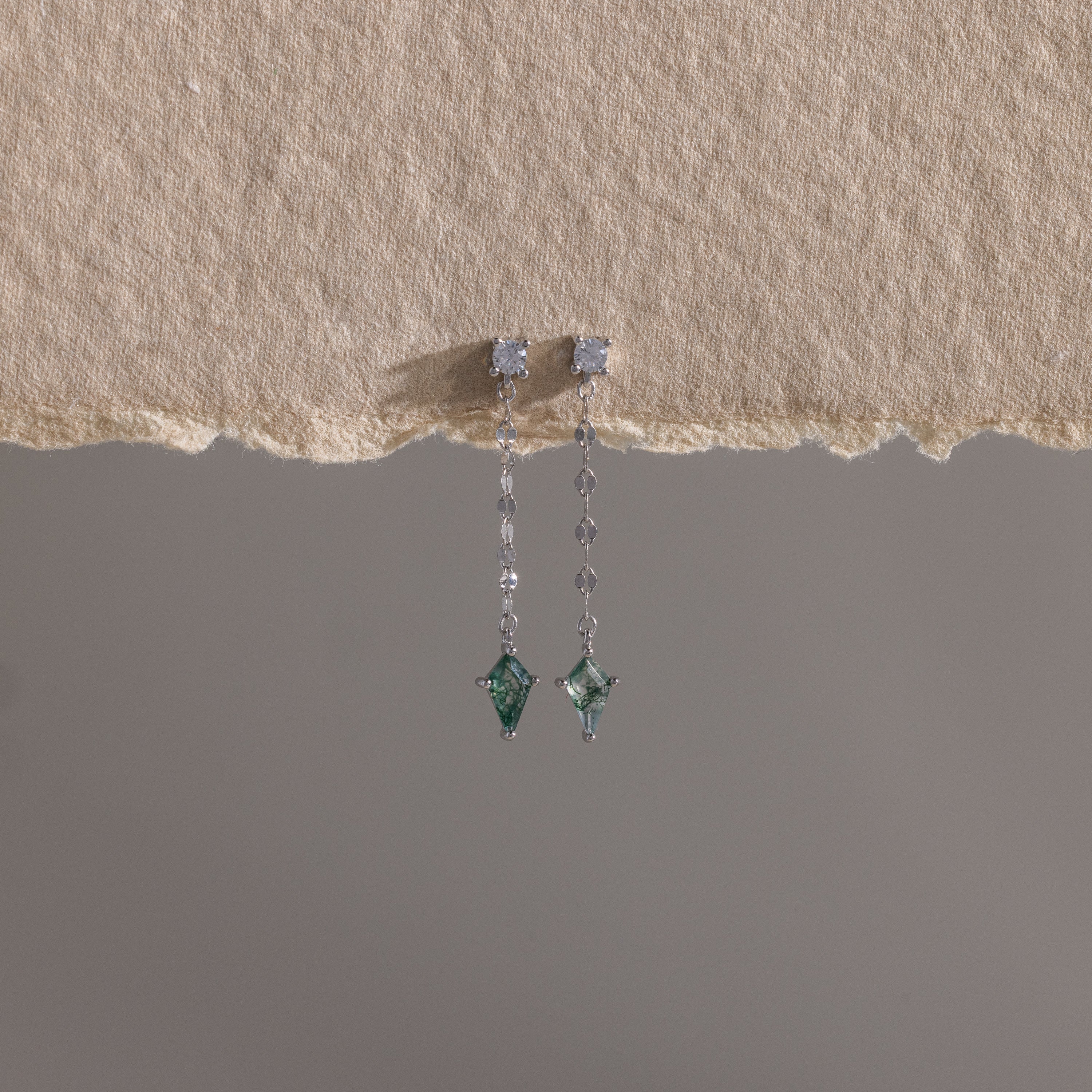 Agate Diamond Dangle Earrings in Sterling Silver featuring green faceted agate stones, shown on textured beige paper with a gray backdrop.