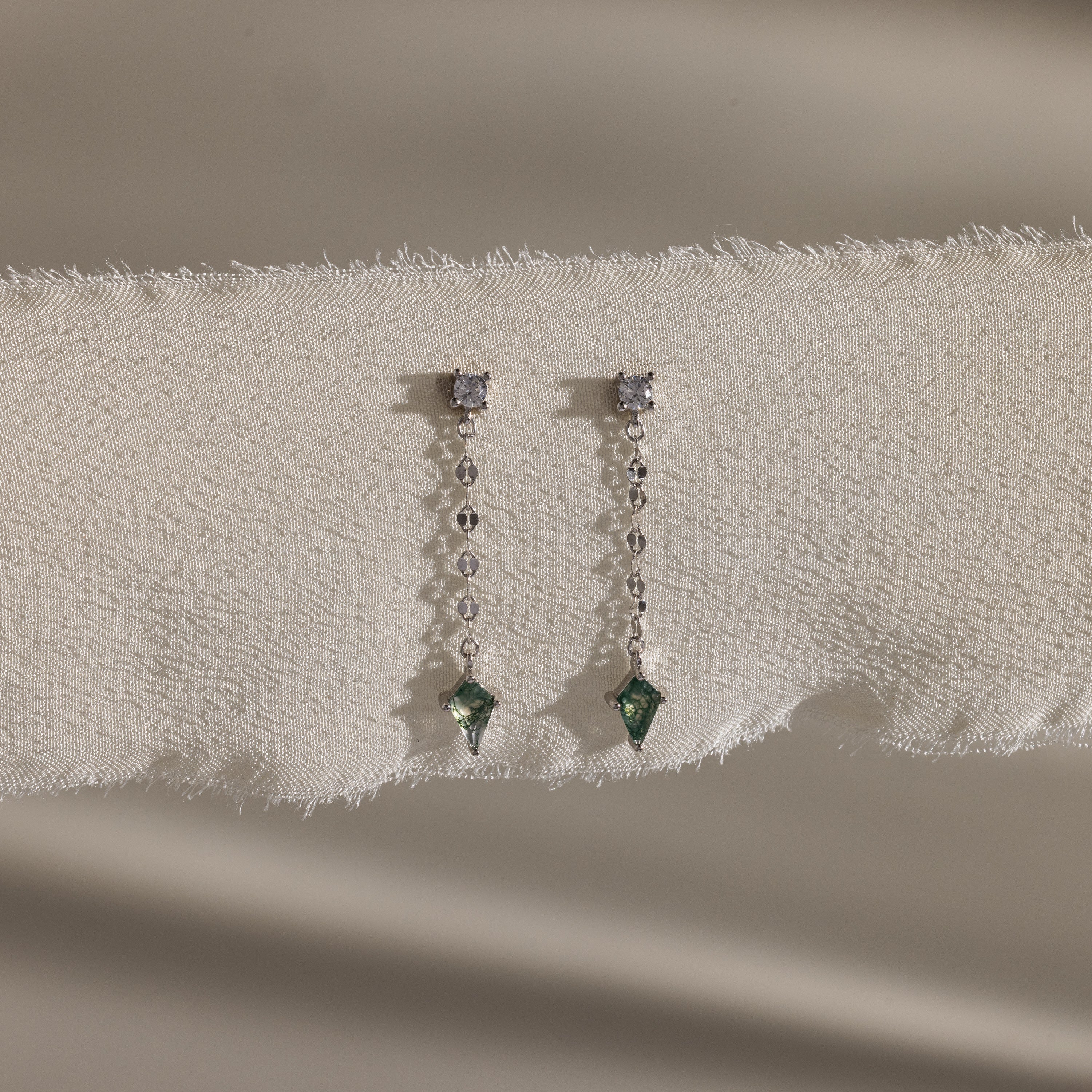 Agate Diamond Dangle Earrings in Sterling Silver, with faceted agate stones, diamonds, and green gemstones on a mirror chain, are elegantly displayed on textured cream fabric.