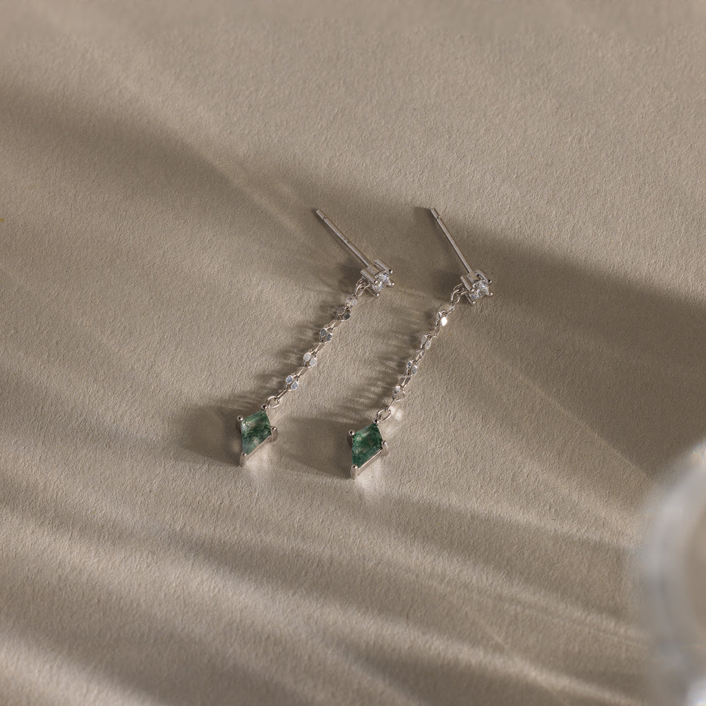 Two elegant Agate Diamond Dangle Earrings in Sterling Silver with green faceted agate stones and small clear accents, displayed on a textured beige surface.