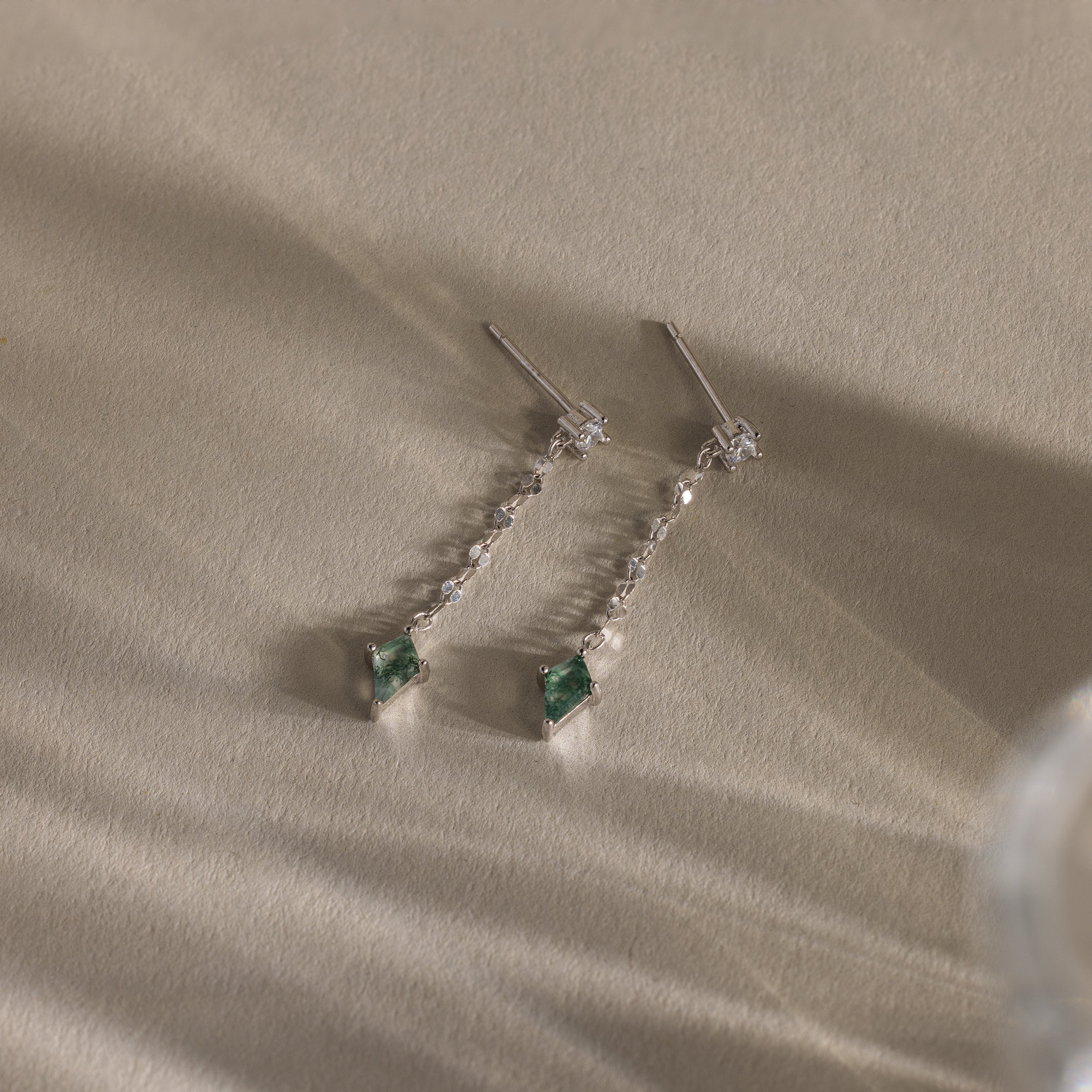 Two elegant Agate Diamond Dangle Earrings in Sterling Silver with green faceted agate stones and small clear accents, displayed on a textured beige surface.