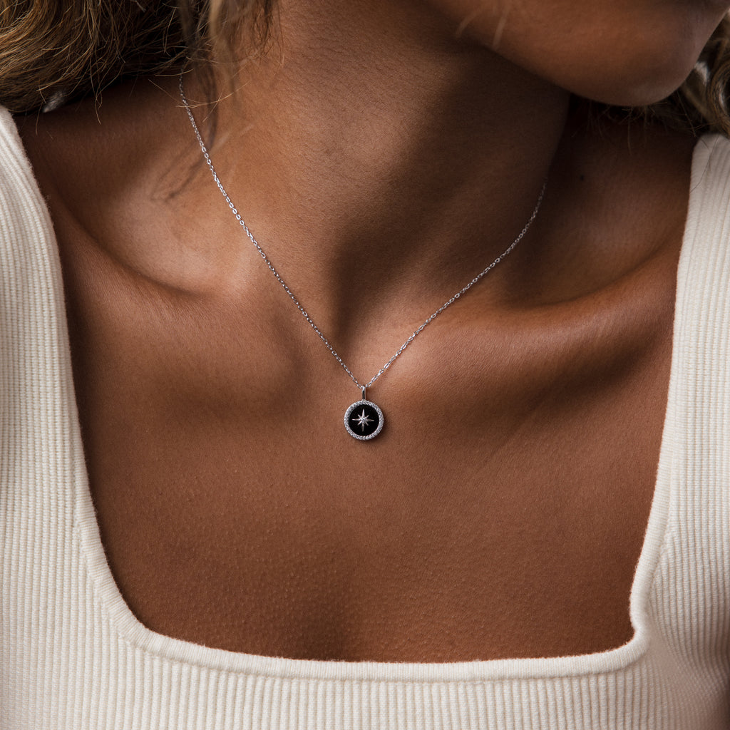 A woman wears the Onyx Star Pendant Necklace, showcasing a circular black onyx pendant with a bold white star design for a celestial touch.