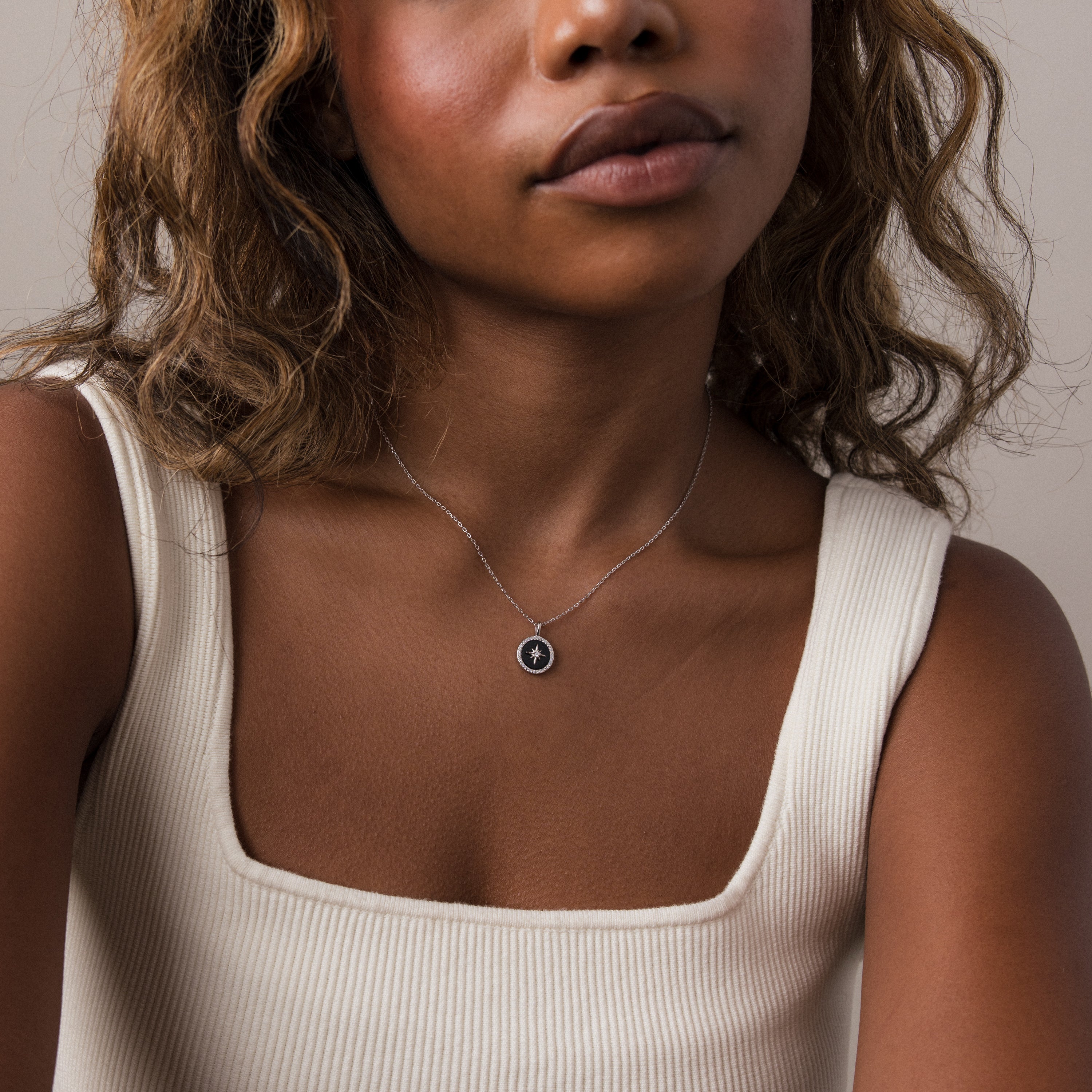 A woman in a cream tank top wears the Onyx Star Pendant Necklace in Sterling Silver, featuring a small round black onyx.