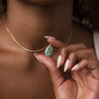 A person holds a Celestial Aventurine Pendant Necklace featuring a gold chain and a teardrop-shaped green aventurine pendant adorned with small gold stars.