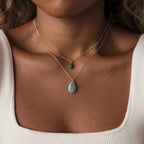 A woman wears two gold necklaces with green gemstone pendants, including a Celestial Aventurine Pendant Necklace, shown close-up against a white ribbed top.