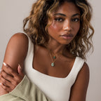 Woman with wavy hair in a white tank top, wearing layered gold necklaces including the Celestial Aventurine Pendant Necklace, and a light green sweater draped over her arm.
