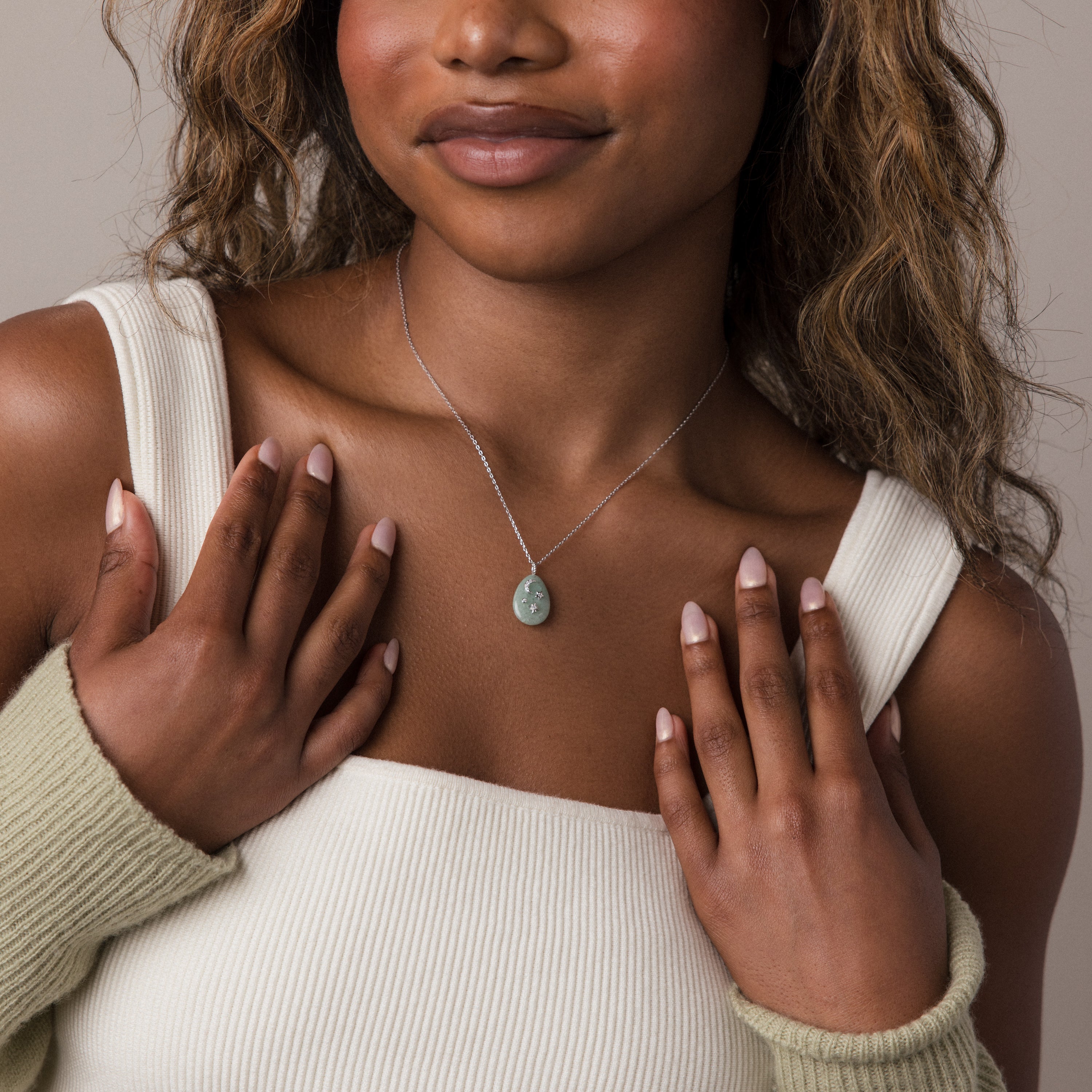 Woman wearing a light top and a Celestial Aventurine Pendant Necklace featuring a green gemstone, with hands gently touching her collarbone.