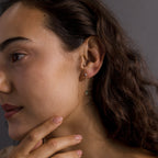 Woman with wavy brown hair wears Agate Diamond Dangle Earrings in 18K Gold, touching her chin thoughtfully.