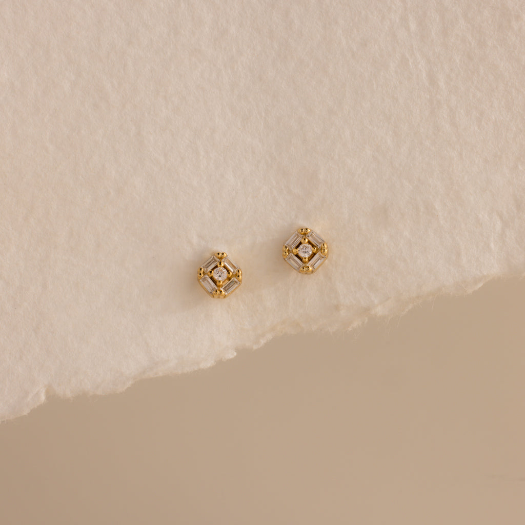 Pair of gold Art Deco flatback earrings with diamond center, styled on torn edge cream paper.
