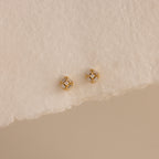 Pair of gold Art Deco flatback earrings with diamond center, styled on torn edge cream paper.