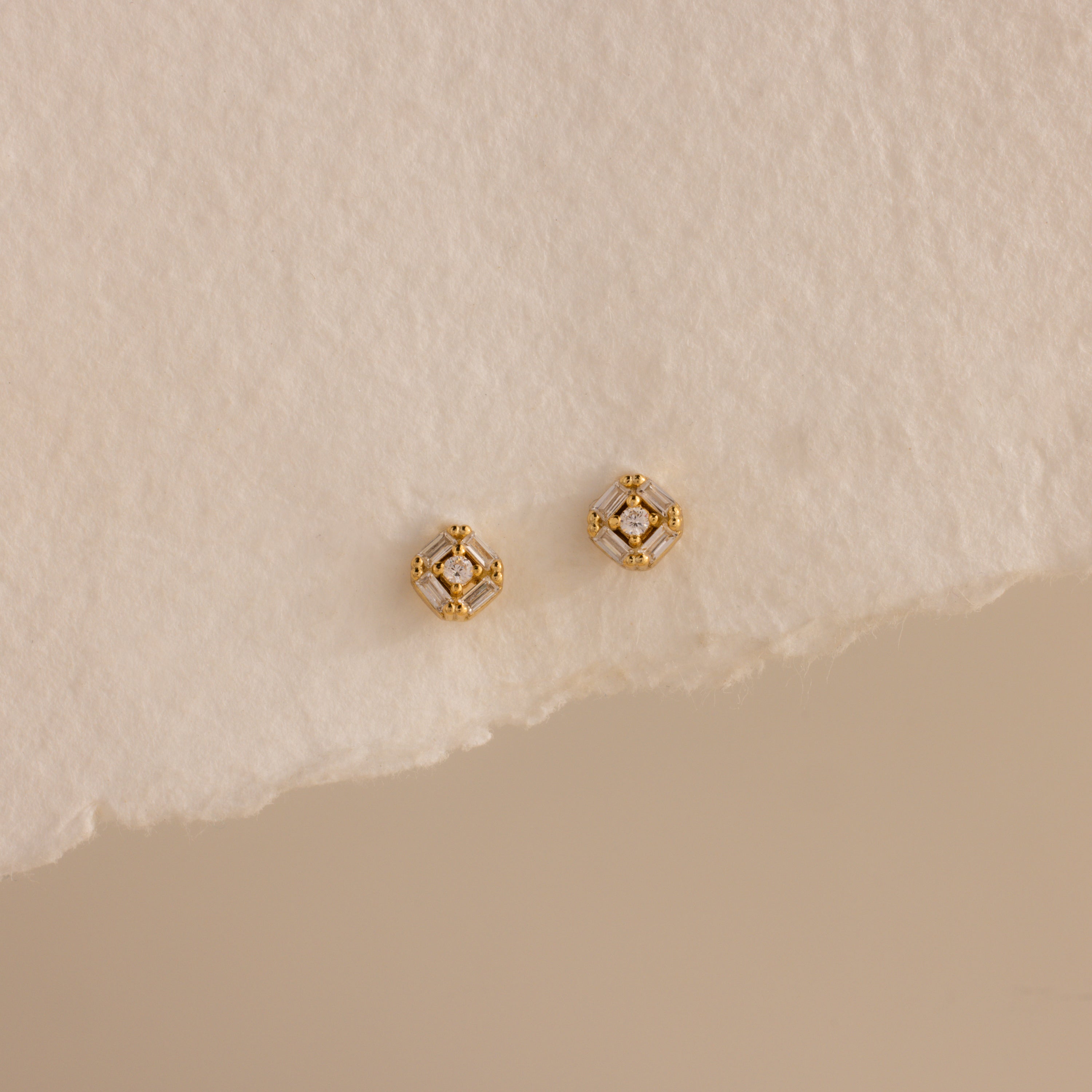Pair of gold Art Deco flatback earrings with diamond center, styled on torn edge cream paper.