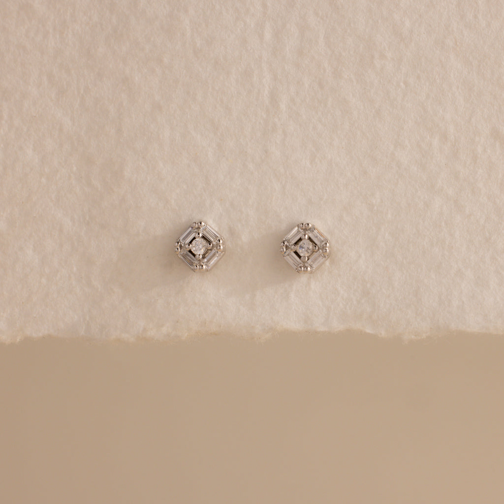 Pair of silver Art Deco flatback earrings with diamond center, styled on torn edge cream paper.