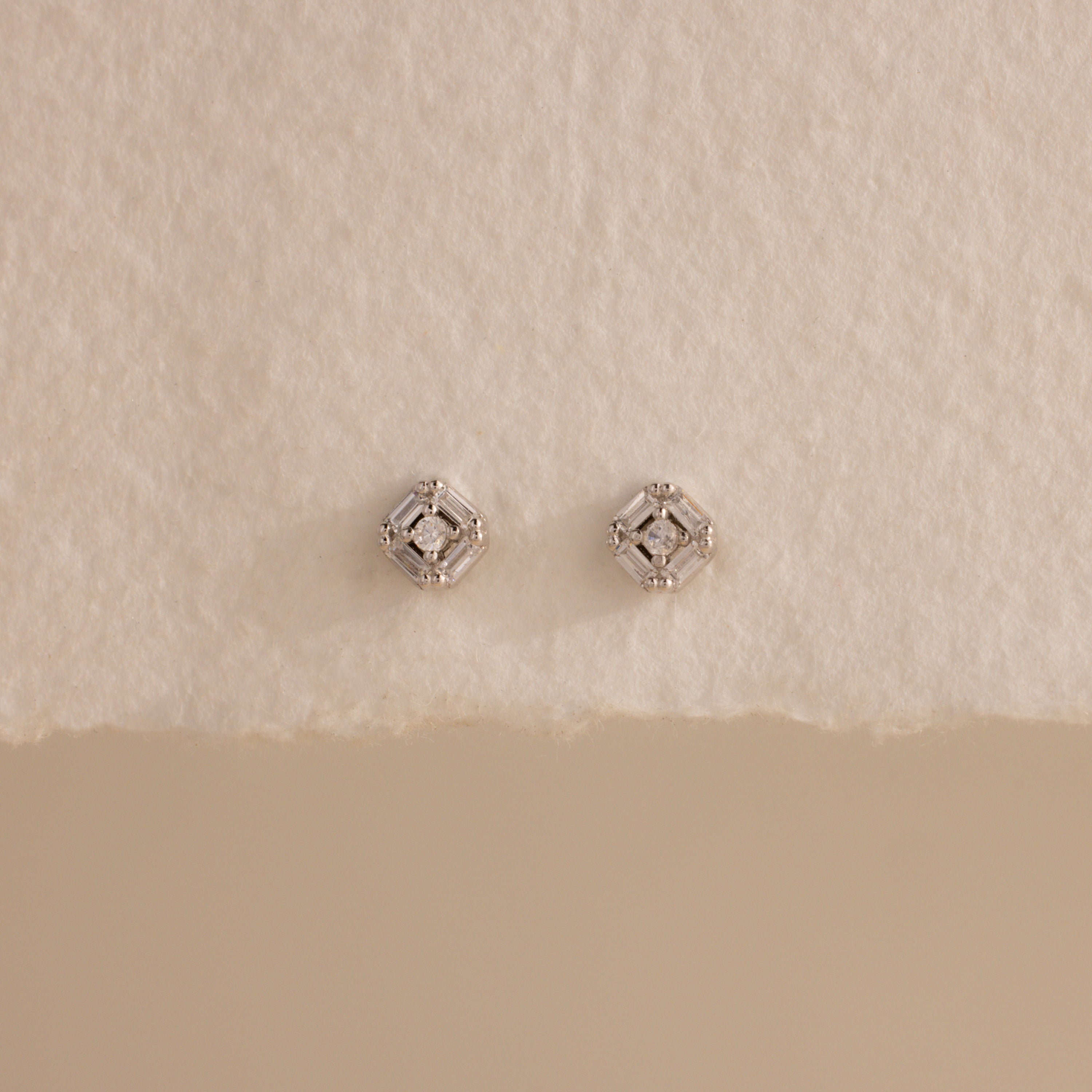 Pair of silver Art Deco flatback earrings with diamond center, styled on torn edge cream paper.
