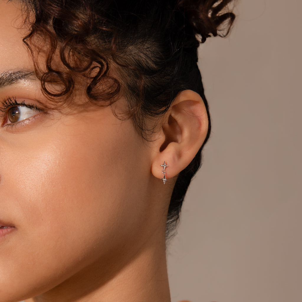 Close-up of a woman wearing minimalist star drop flatback earrings on her lobe.