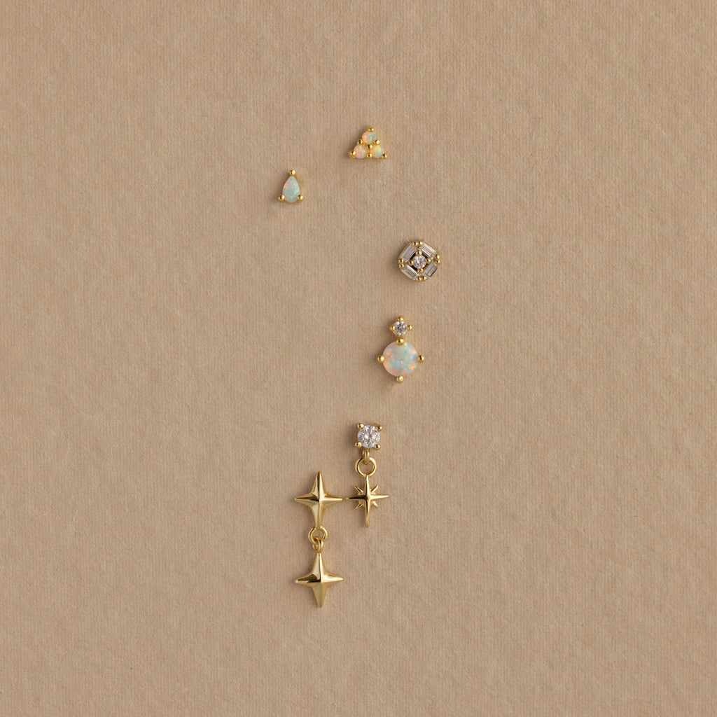 Six Opal  Diamond Flatback Studs in 18K Gold, featuring various designs like stars and gems, are arranged vertically on a beige background.
