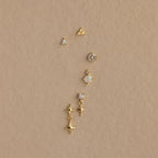 Six Opal  Diamond Flatback Studs in 18K Gold, featuring various designs like stars and gems, are arranged vertically on a beige background.