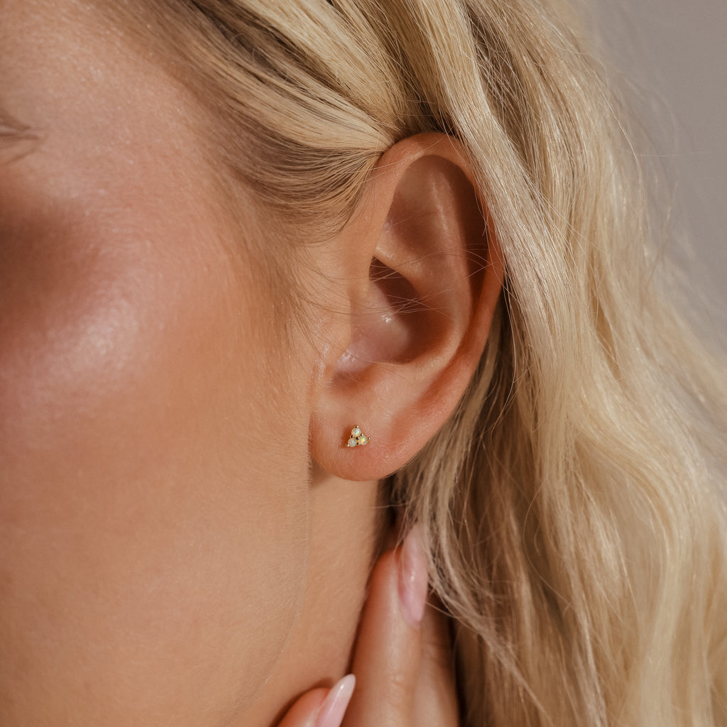 A close-up of a woman's ear showing a single silver Opal Cluster Stud Earring worn on the lobe, capturing its small, triangular shape and opal shimmer.