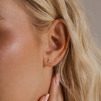 A close-up of a woman's ear showing a single silver Opal Cluster Stud Earring worn on the lobe, capturing its small, triangular shape and opal shimmer.