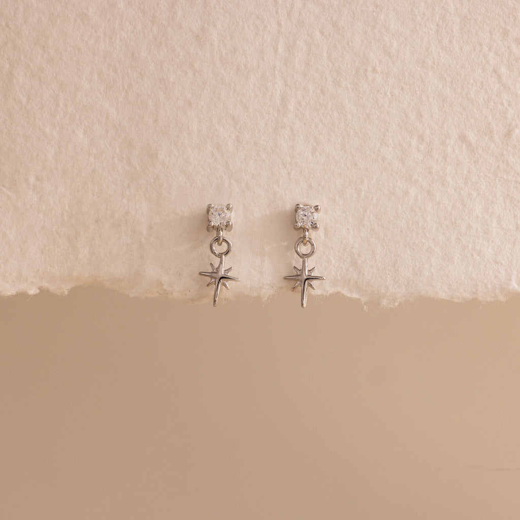 A straight-on product display of the 18k silver Diamond Star Flatback Earrings against a soft beige and off-white background, highlighting the charm's clean symmetry.