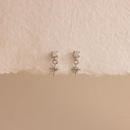 A straight-on product display of the 18k silver Diamond Star Flatback Earrings against a soft beige and off-white background, highlighting the charm's clean symmetry.