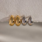 Four Bold Teardrop Earrings—two gold and two silver—are displayed on a white textured surface, highlighting modern jewelry with a striking flair.