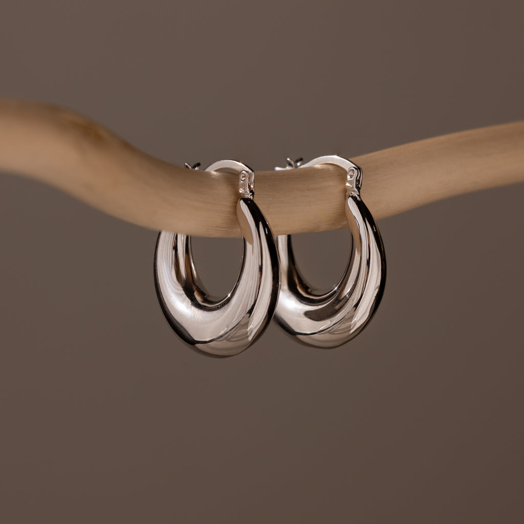 Sculpted Hoops in White Gold with a high shine finish hang elegantly on a smooth, light-colored branch against a neutral background.