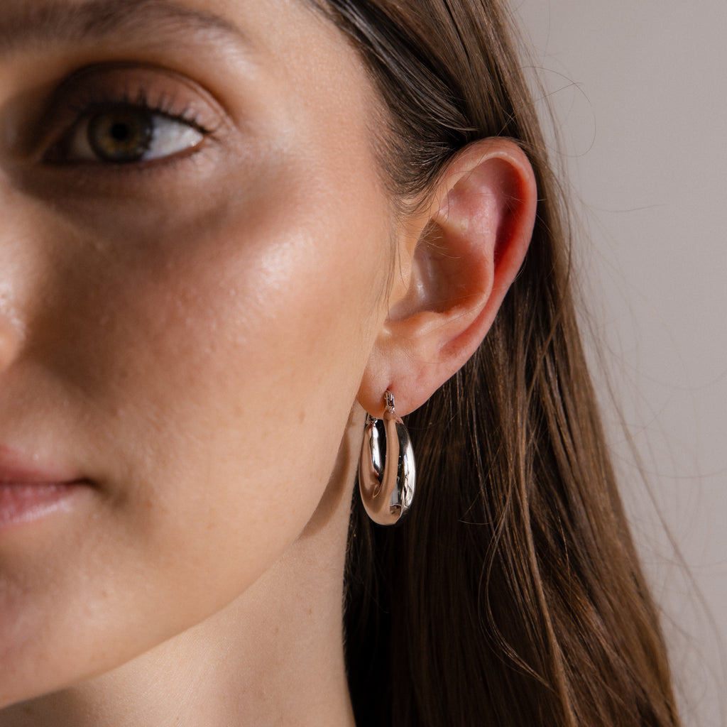 Close-up of a woman with long brown hair wearing Sculpted Hoops in White Gold—shiny white gold earrings on her left ear for a high-shine finish.