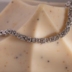 A Bold Byzantine Bracelet in White Gold draped over a geometric, speckled beige soap bar adds a touch of luxury jewelry to your daily essentials.