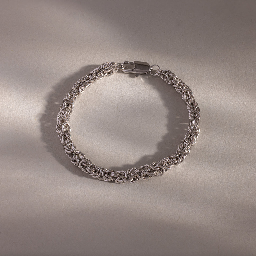 A luxury jewelry piece, the Bold Byzantine Bracelet in White Gold showcases intricate links, elegantly presented on a neutral, softly lit surface.
