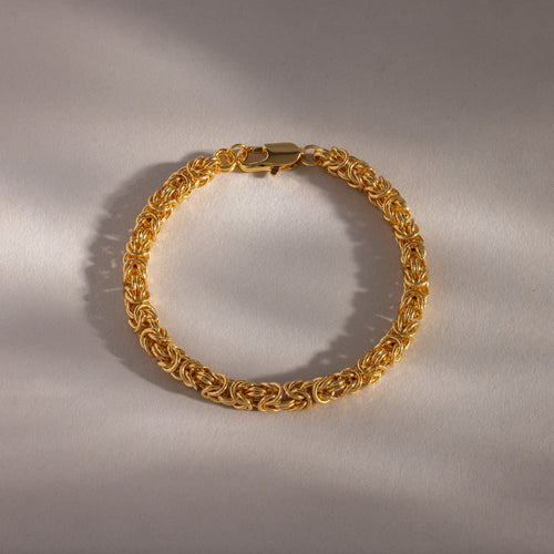 The Bold Byzantine Bracelet in 18K Gold features woven links and intricate detailing, displayed on a neutral background with soft lighting for an elegant touch.