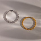 The Bold Byzantine Bracelet—available in silver and gold—features woven textured links and is displayed on a light, neutral background, showcasing quiet luxury.