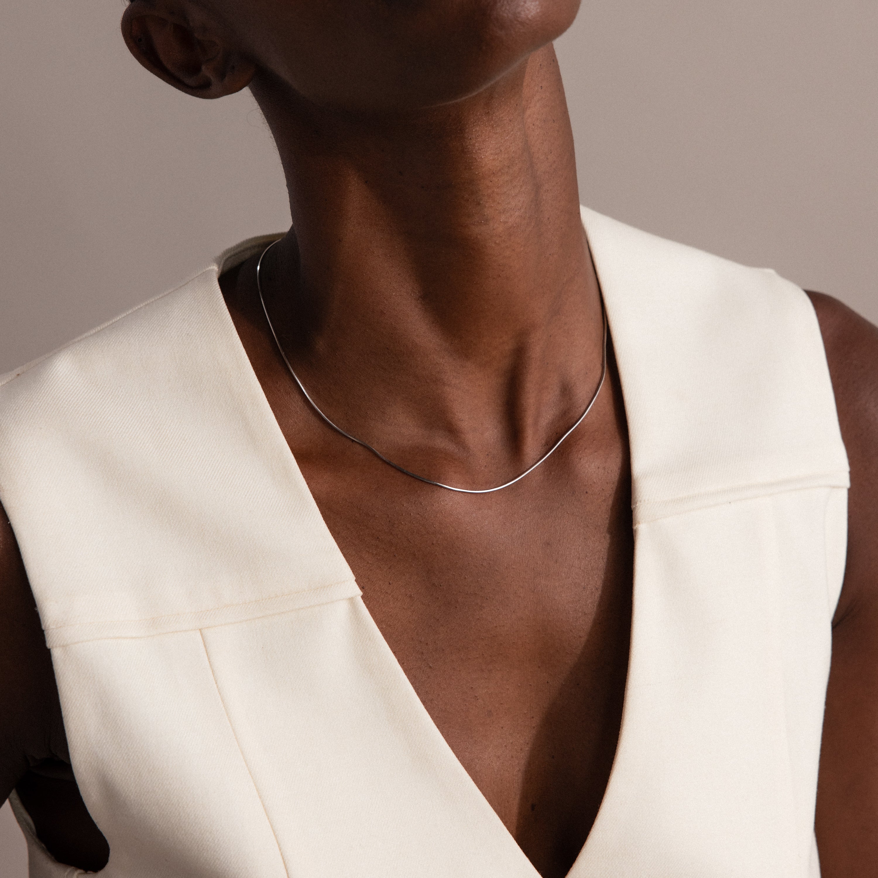 A person wearing a cream sleeveless top and the Dainty Herringbone Necklace in Sterling Silver, head tilted back.