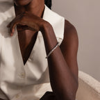 A woman in a sleeveless white top wears a striking Byzantine Link Bracelet in White Gold with an interwoven design, resting her chin on her hand.