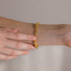 A hand wearing and adjusting the Bold Byzantine Bracelet in 18K Gold with woven links against a neutral background, embodying quiet luxury.