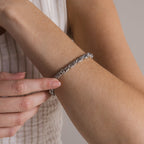 A person wearing the Bold Byzantine Bracelet in White Gold on their wrist, gently touching it with their other hand—ideal for those who appreciate luxurious jewelry.