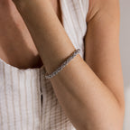 A person wears the Bold Byzantine Bracelet in White Gold on their wrist, paired with a sleeveless, striped white linen top.