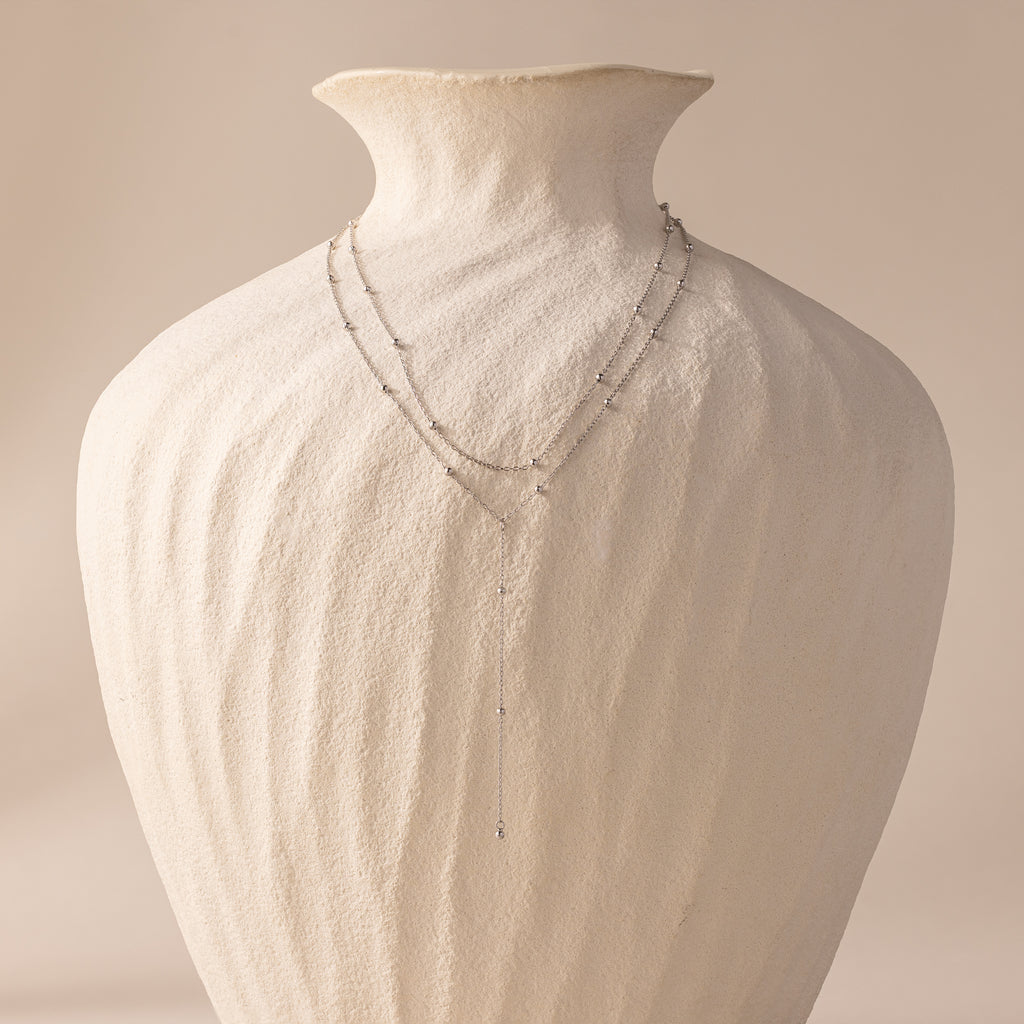 Silver satellite lariat necklace displayed on a sculptural ivory vase, showing full length and layered design.