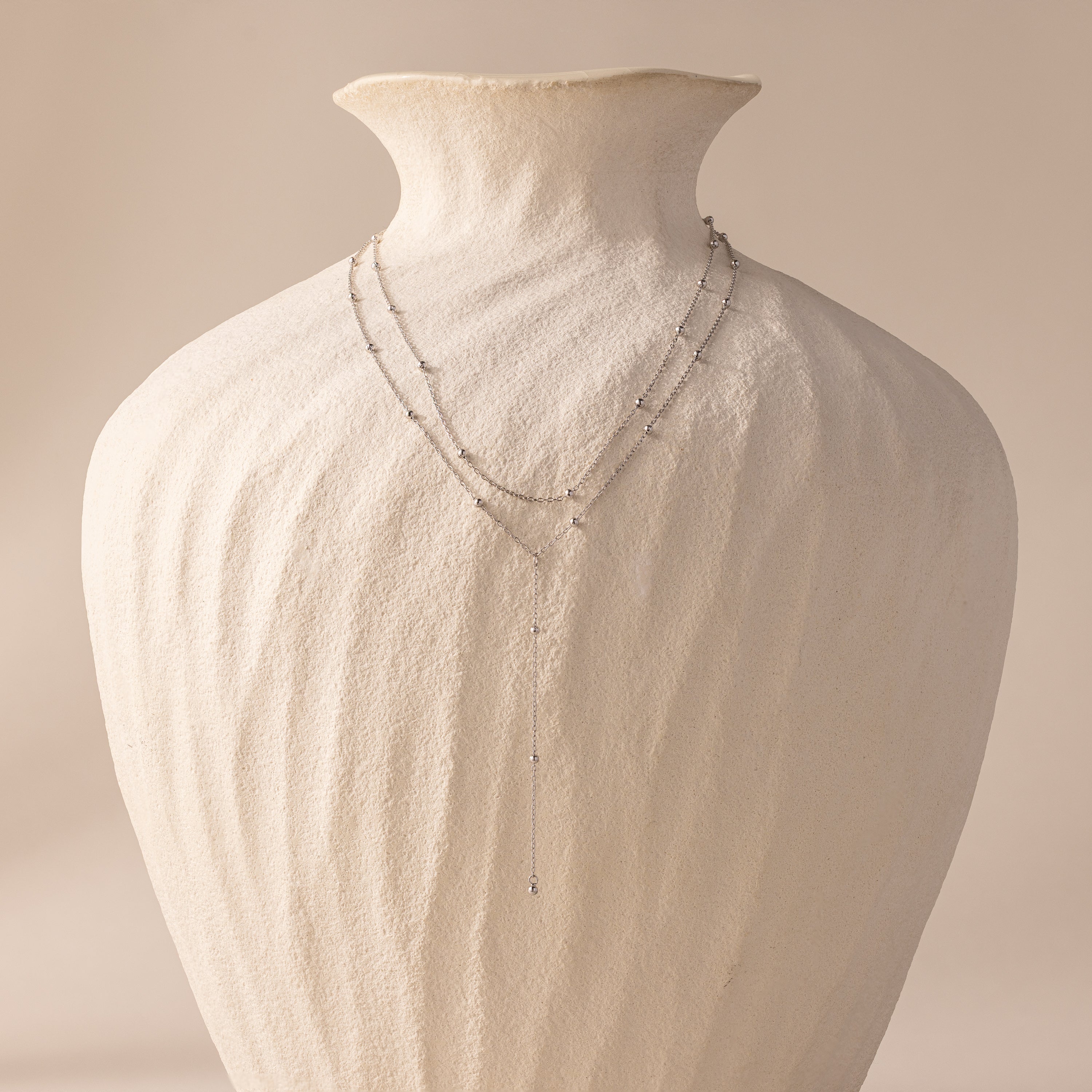 Silver satellite lariat necklace displayed on a sculptural ivory vase, showing full length and layered design.