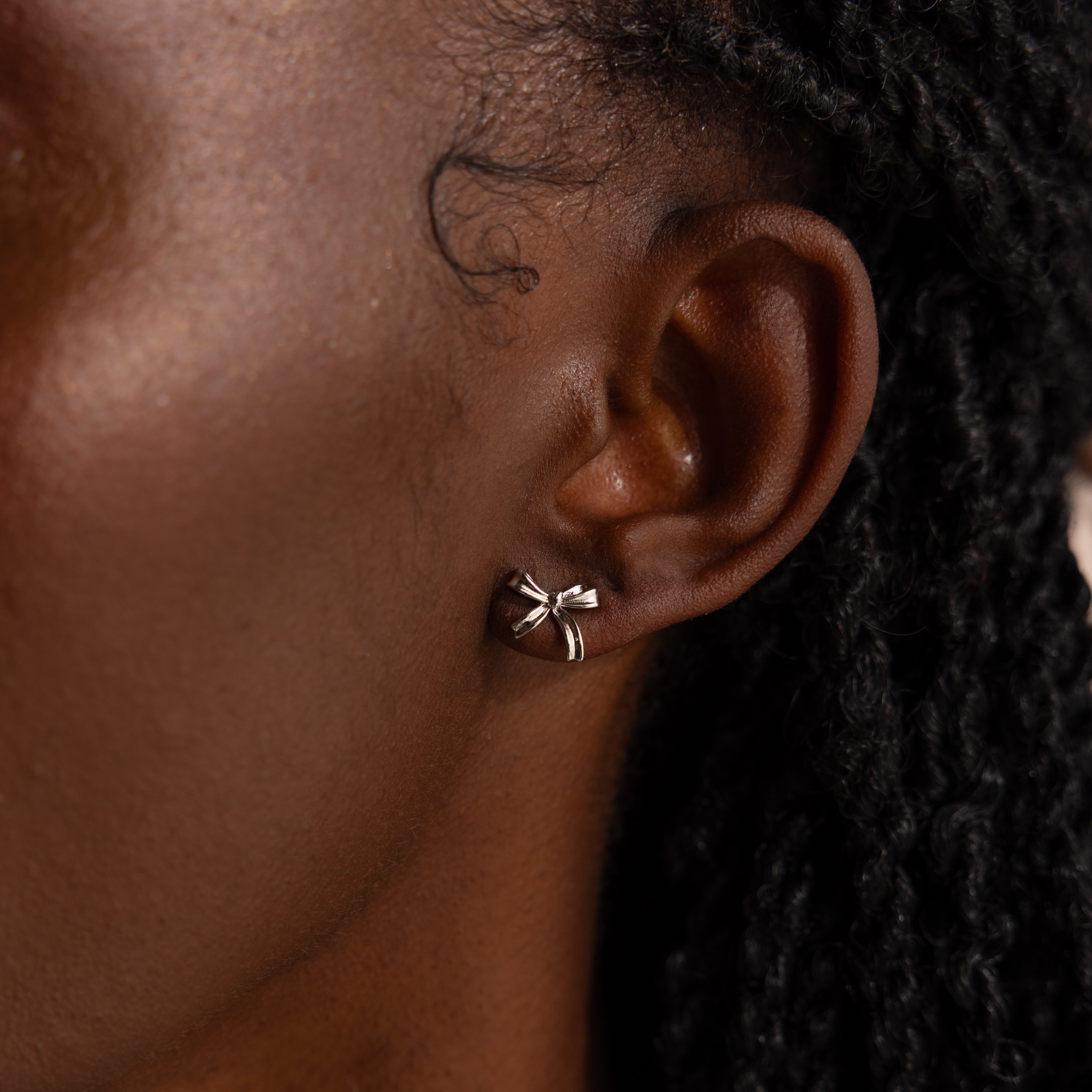Up-close of model wearing dainty silver bow stud earrings.