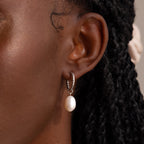 Close-up of a model wearing a twisted silver hoop earring with a single dangling freshwater pearl.