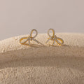 Gold bow-shaped stud earrings encrusted with sparkling cubic zirconia, displayed on a textured neutral surface with soft lighting.