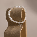 Elegant pearl bracelet with dainty silver bow charm displayed on a sculpted neutral-toned stand.