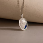 The Organic Fingerprint Multi Birthstone Necklace in Sterling Silver features an oval pendant with two small blue gemstones on a delicate chain—a personalized, elegant keepsake and perfect birthstone necklace.