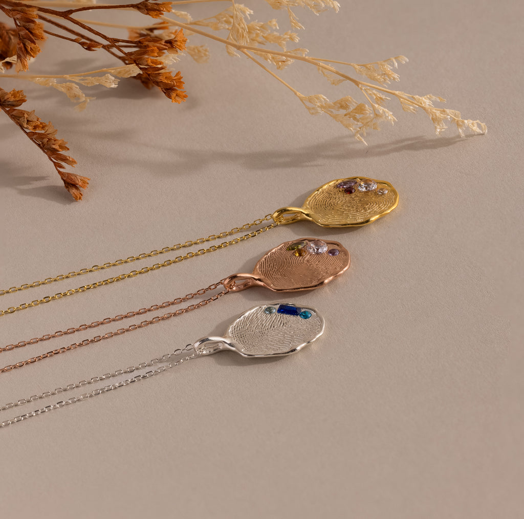 The Organic Fingerprint Multi Birthstone Necklace features textured metal pendants in gold, rose gold, and silver on chains—ideal as a personalized keepsake or unique family necklace.
