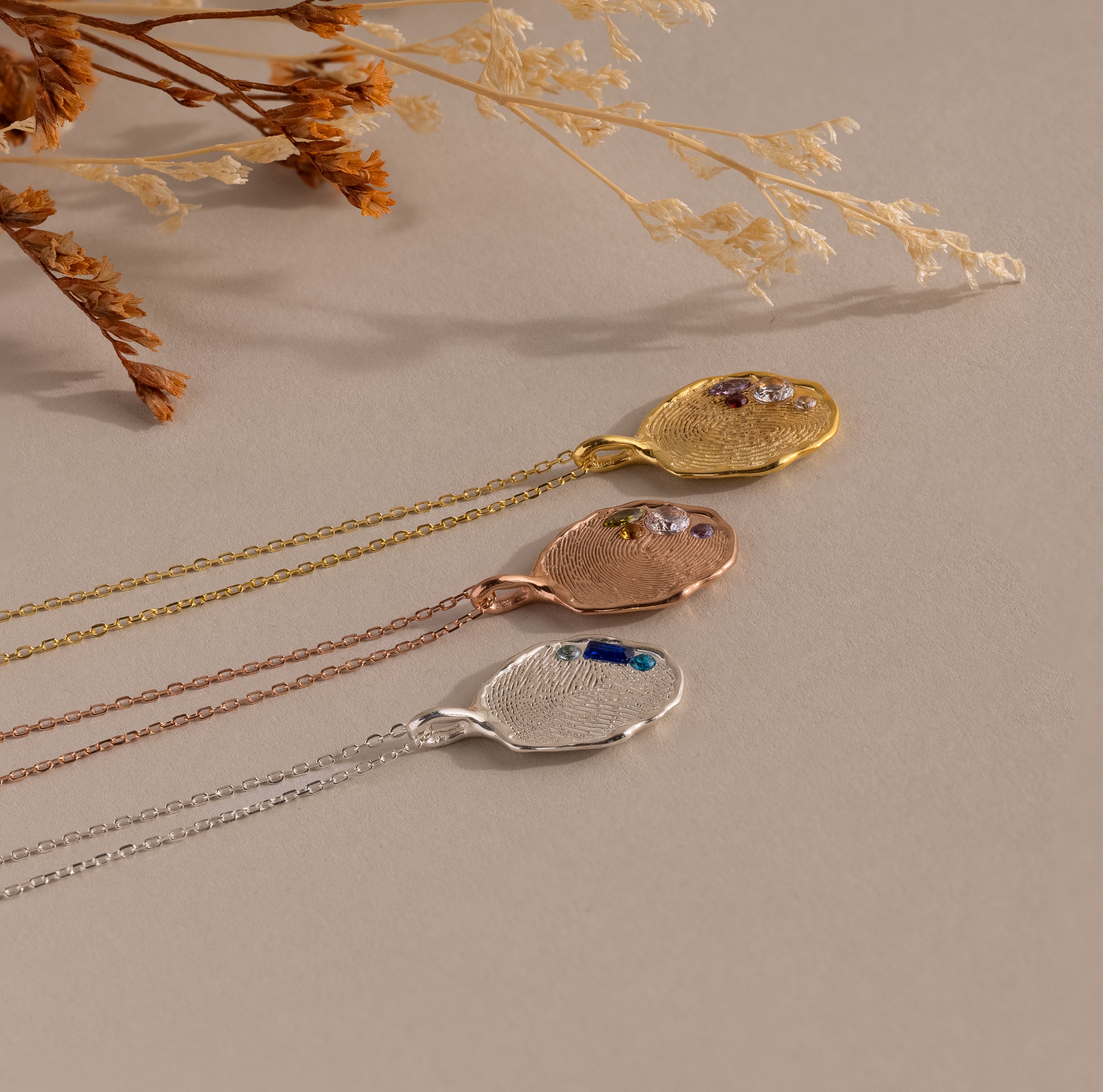 The Organic Fingerprint Multi Birthstone Necklace features textured metal pendants in gold, rose gold, and silver on chains—ideal as a personalized keepsake or unique family necklace.